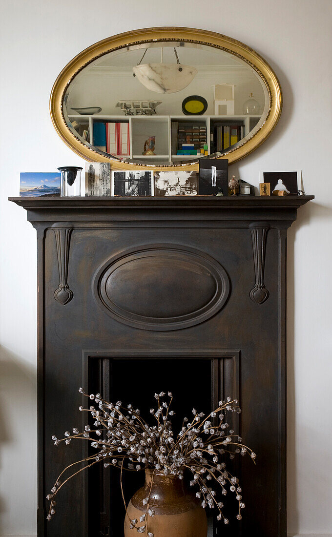 Fireplace with flower arrangement and postcards on the mantlepiece and mirror reflecting storage unit