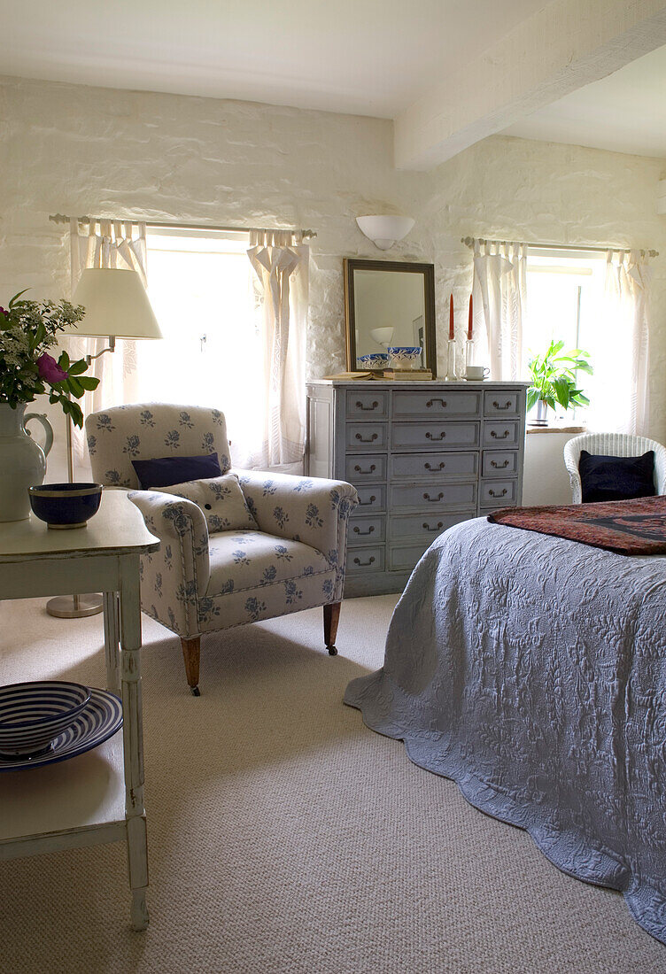 Floral patterned armchair in whitewashed bedroom of mill conversion