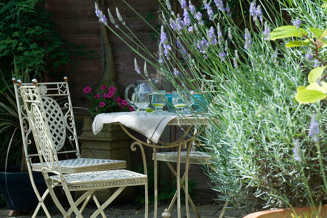 White ornamental metal garden furniture and water jug and glasses with flowering lavender