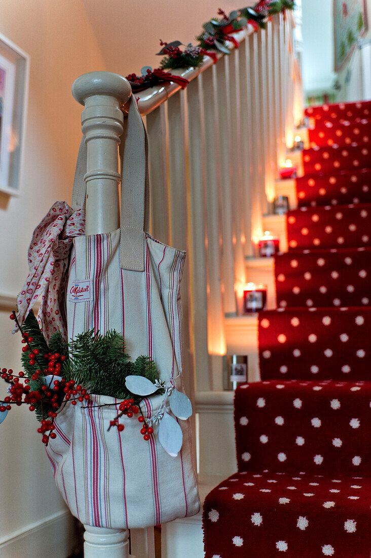 Christmas decorations in bag on banister of candlelit staircase in London home UK