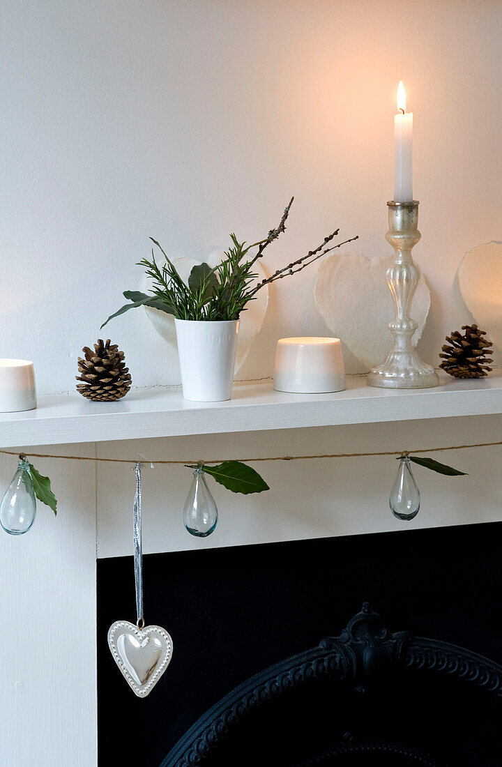 Lit candle and pinecones with glass ornaments on original fireplace of London home 