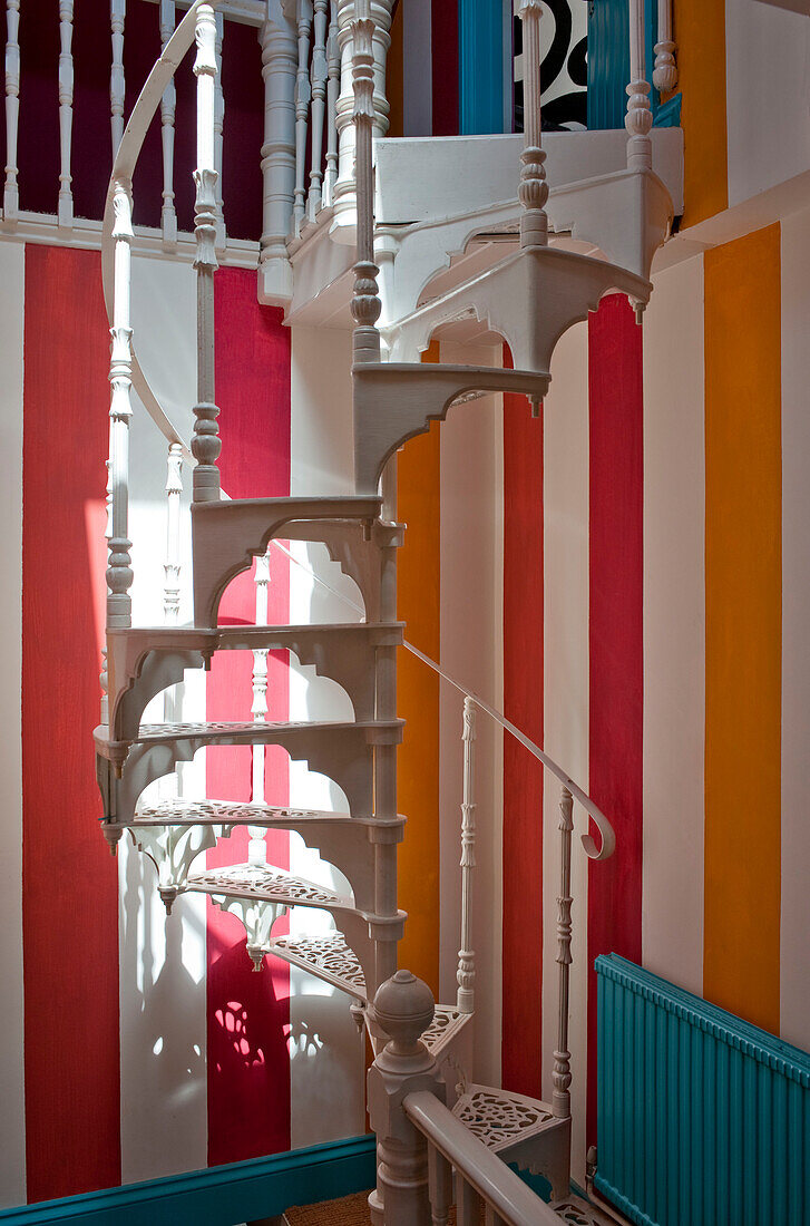 Wrought iron white painted spiral staircase with colourful stripey wallpaper in UK home