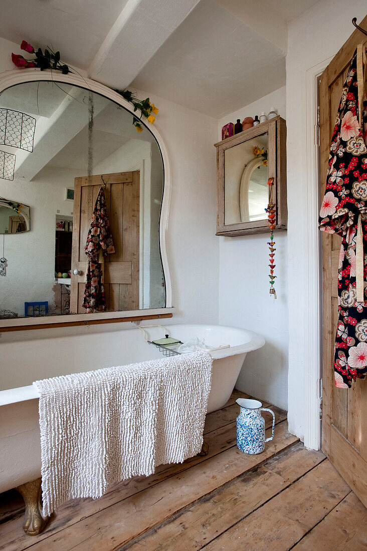Spiegel über freistehender Badewanne mit Kimono auf der Rückseite der Tür in einem Haus in Großbritannien