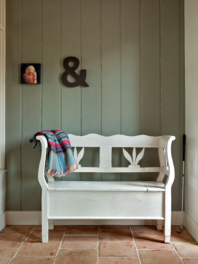 Ampersand an getäfelter Wand mit Kunstwerk über einer weiß gestrichenen Gartenbank in einem Familienhaus in Suffolk, England, UK