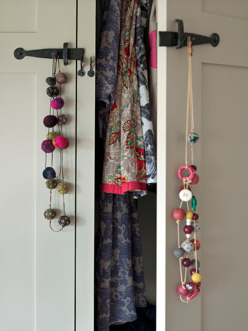 Perlenschmuck hängt an der Türklinke eines offenen Kleiderschranks mit geblümter Kleidung in einem Einfamilienhaus in Suffolk England UK