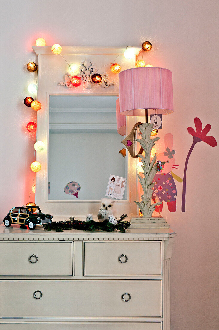 Lit lamps around mirror on chest of drawers in girl's room in Paris apartment, France