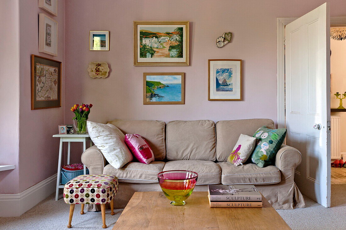 Kunstwerke über dem hellbraunen Sofa im rosa Wohnzimmer des Hauses der Familie Bovey Tracey, Devon, England, UK