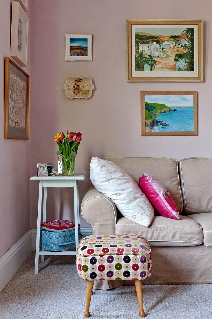 Artwork display above brown sofa with upholstered footstool in living room of Bovey Tracey family home, Devon, England, UK