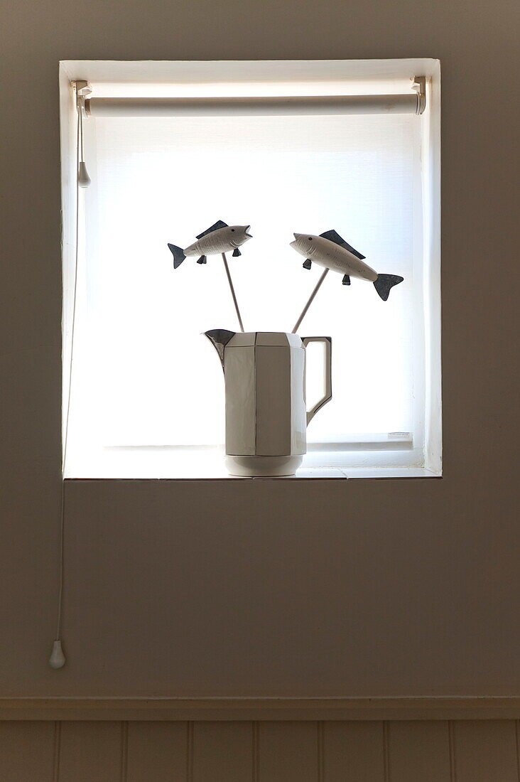 Backlit model fish in jug on windowsill with roller blinds in Suffolk farmhouse, England, UK
