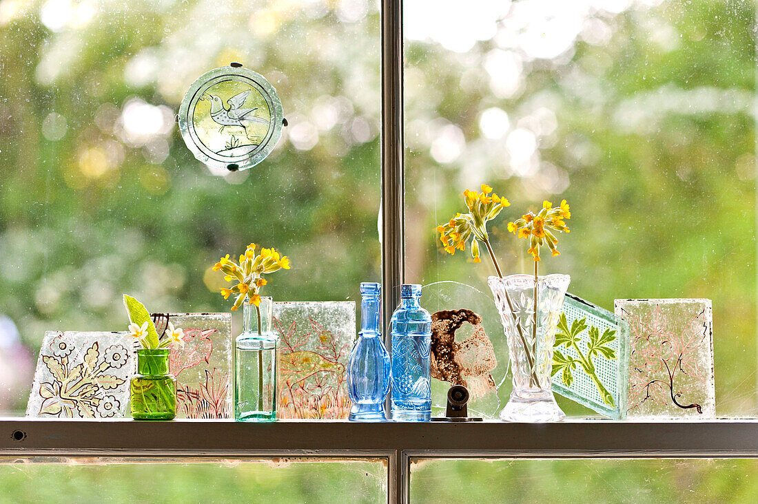 Einstämmige Blumen in kleinen Vasen mit handgemalten Glasmalereien im Fenster eines Hauses in Essex, England, UK