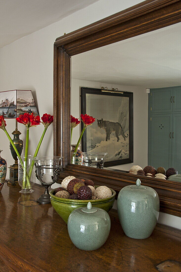 Schnittblumen und Ornamente auf Sideboard mit holzgerahmtem Spiegel in modernem Landhaus in Suffolk, England, UK