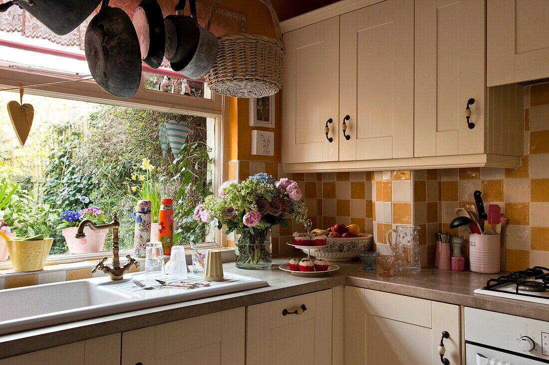 Draining board at window of kitchen with white fitted units and checked splashback in London home, England, UK