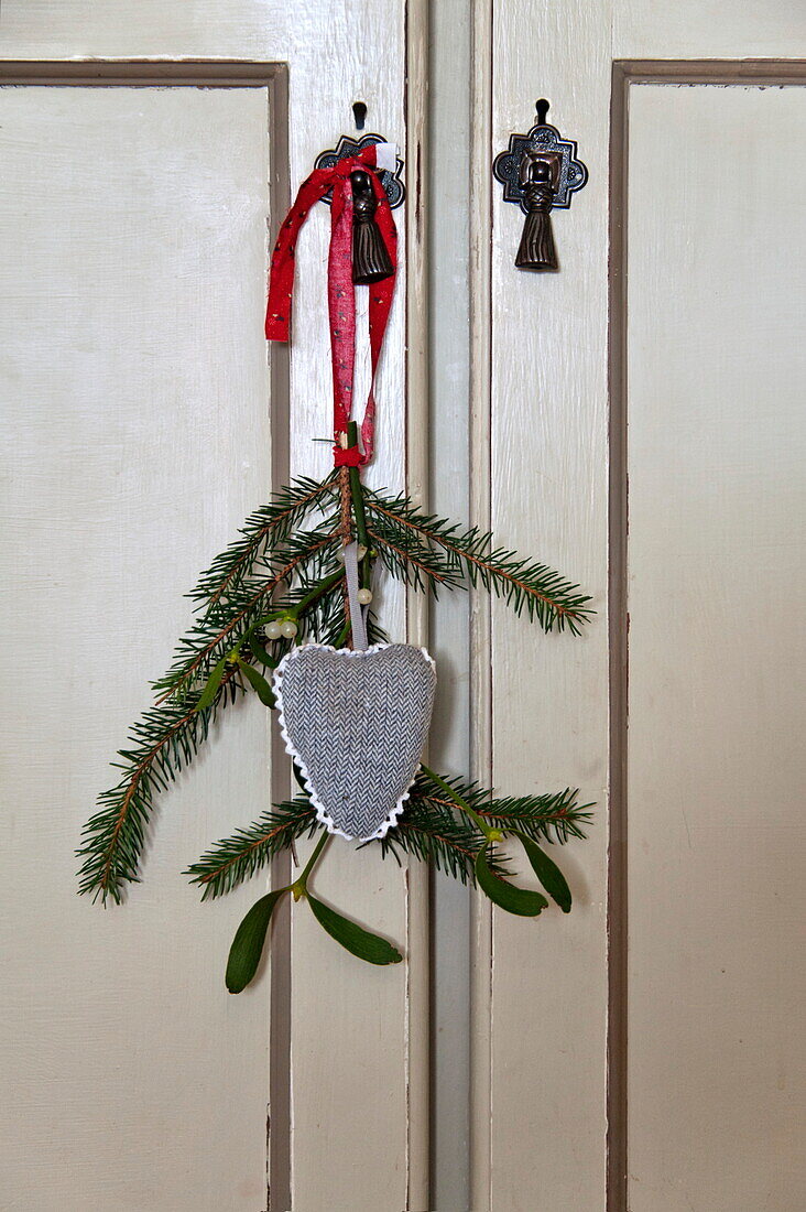 Heart shaped decoration with sprig of mistletoe and pine on cupboard door in Shropshire cottage, England, UK