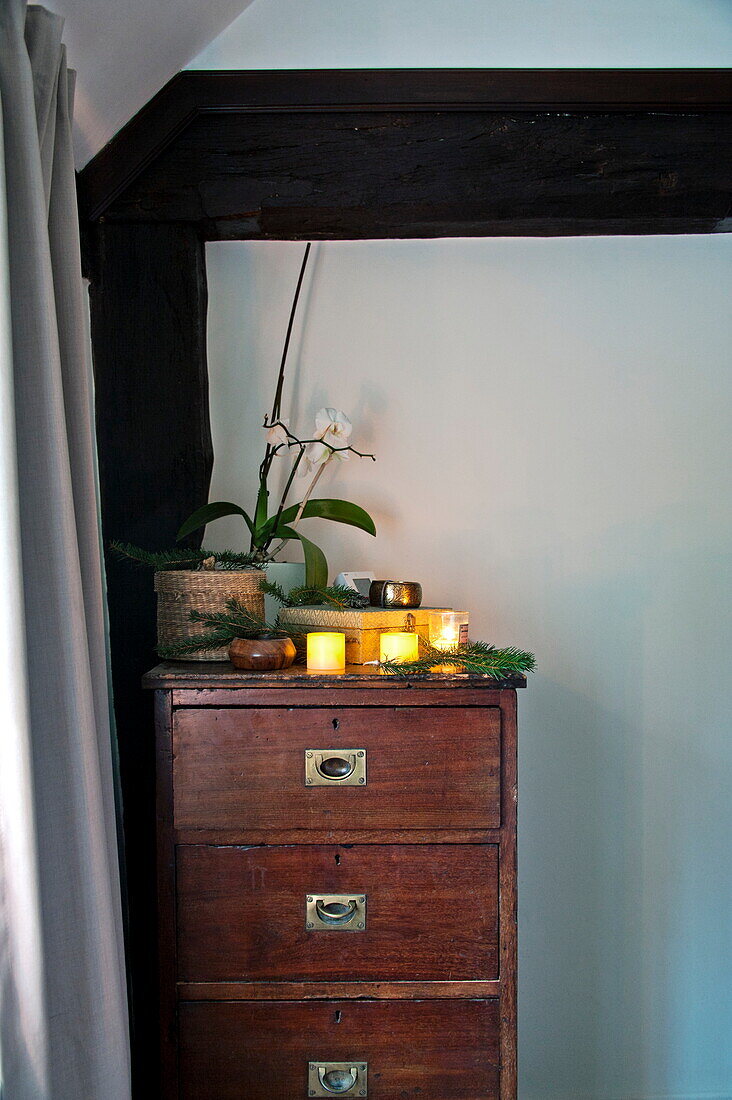 Lit candles and orchid on wooden chest of drawers in Shropshire cottage, England, UK