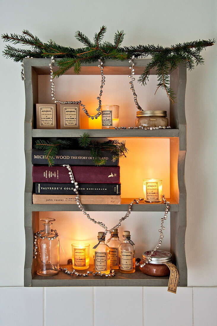 Lit candles and books on wall mounted shelf with Christmas decoration in Shropshire cottage, England, UK