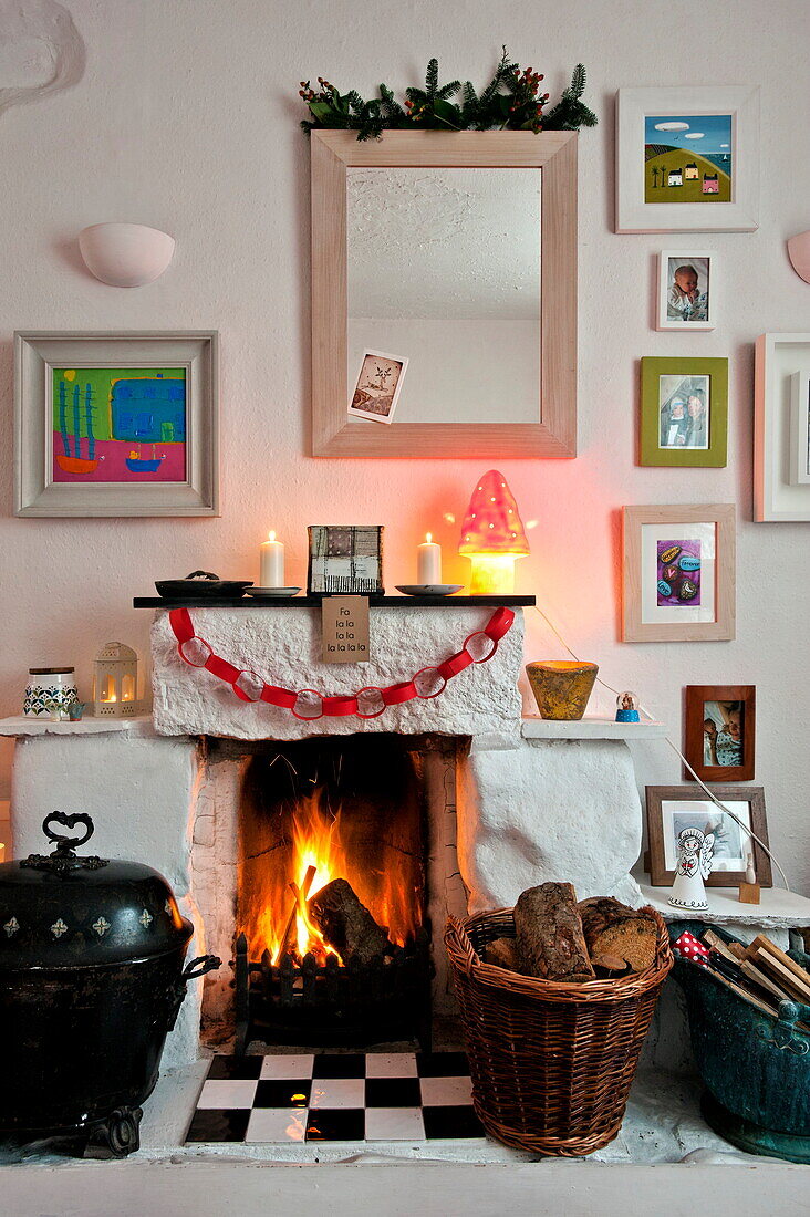 Kohleeimer und Korb mit Holzscheiten vor einem beleuchteten Kamin in einem Haus in Penzance, Cornwall, England