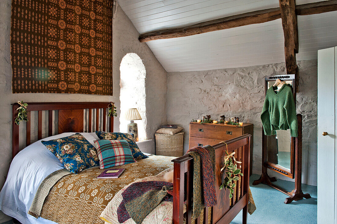 Gold and red wall hanging above wooden bed in whitewashed bedroom of Tregaron home Wales UK