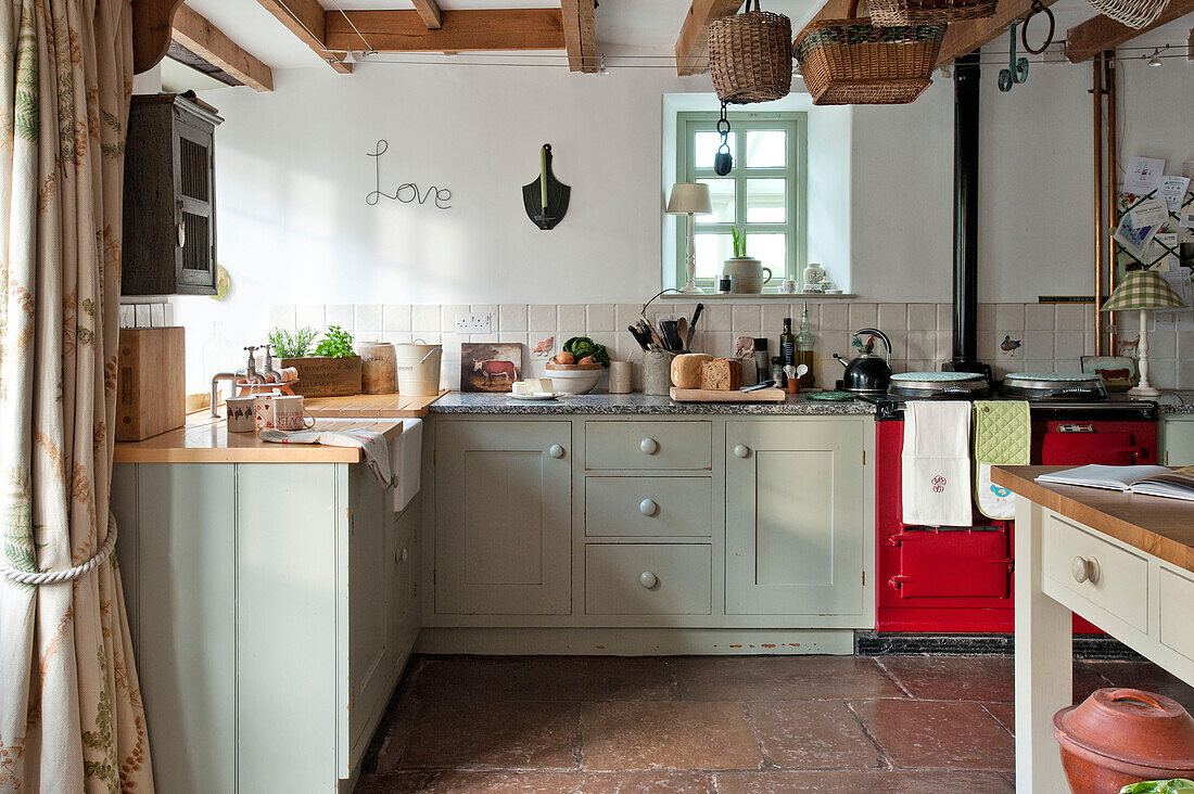 Light green fitted kitchen with small window and flagstone flooring in Sherford barn conversion Devon UK