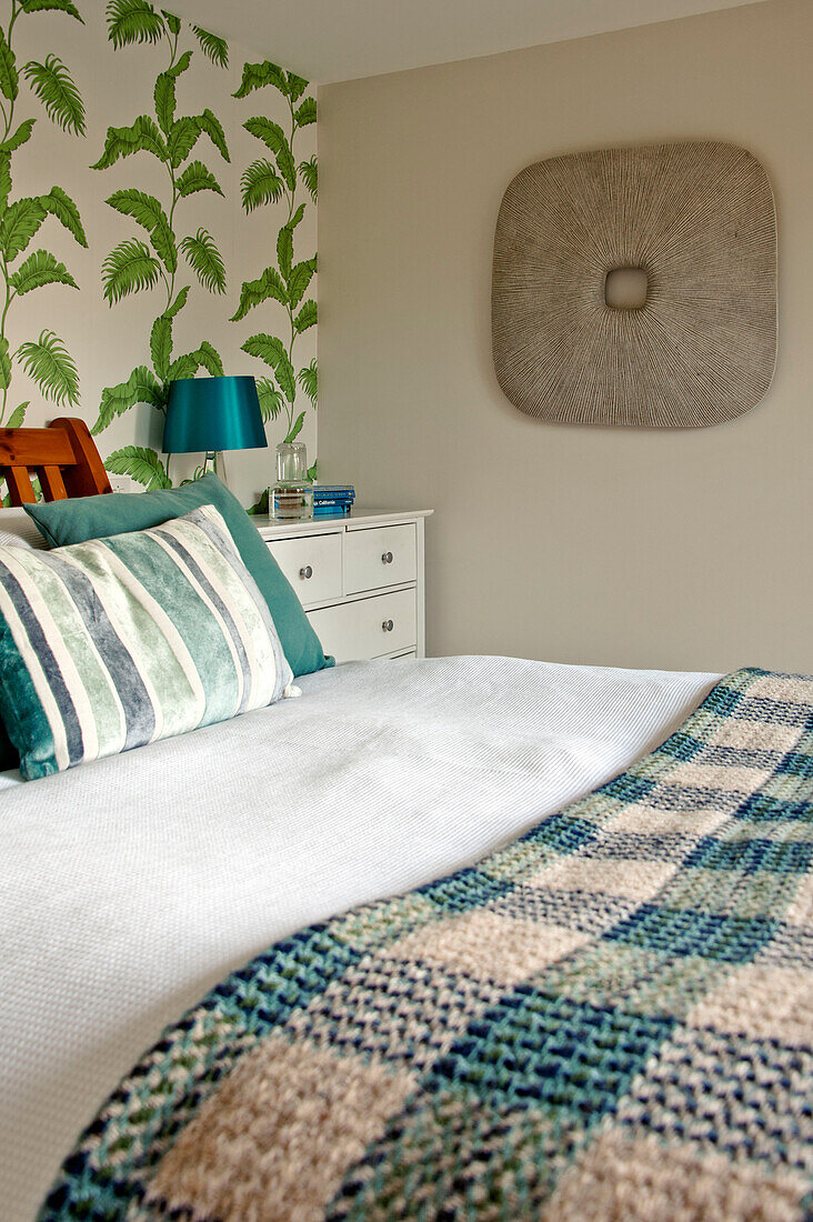 Checked blanket on double bed in room with leaf patterned wallpaper in Cornwall home UK