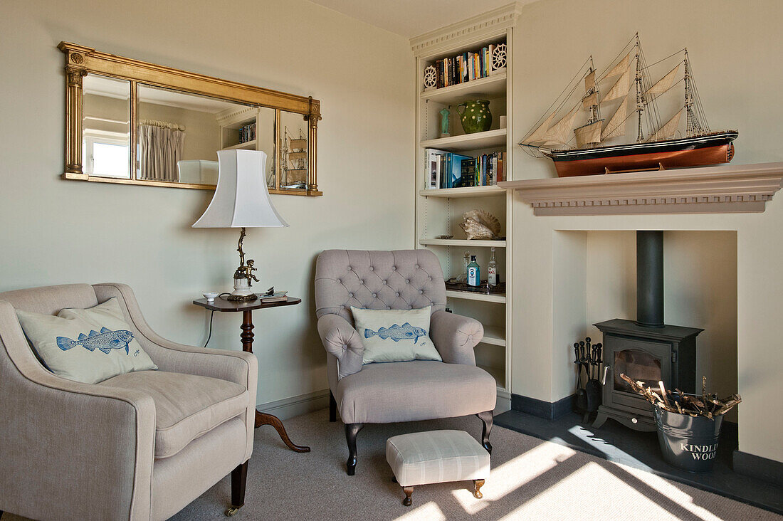 Model ship on mantlepiece with gilt framed mirror and armchairs in living room of family home, Cornwall, UK