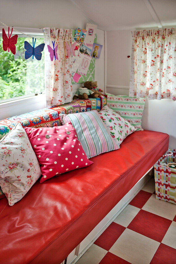 Assorted cushions with floral curtains and butterfly decoration above red bench seat in caravan