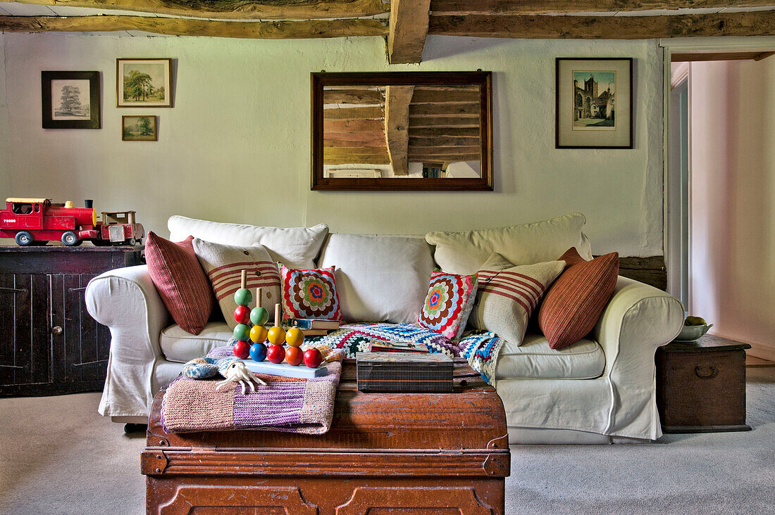 Child's toys on travelling trunk with white sofa in beamed living room of Cambridge cottage England UK