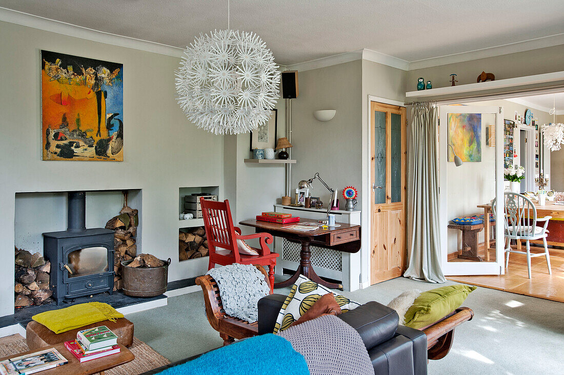 Large pendant shade hangs in living room with red painted chair and woodburning stove East Grinstead family home West Sussex England UK