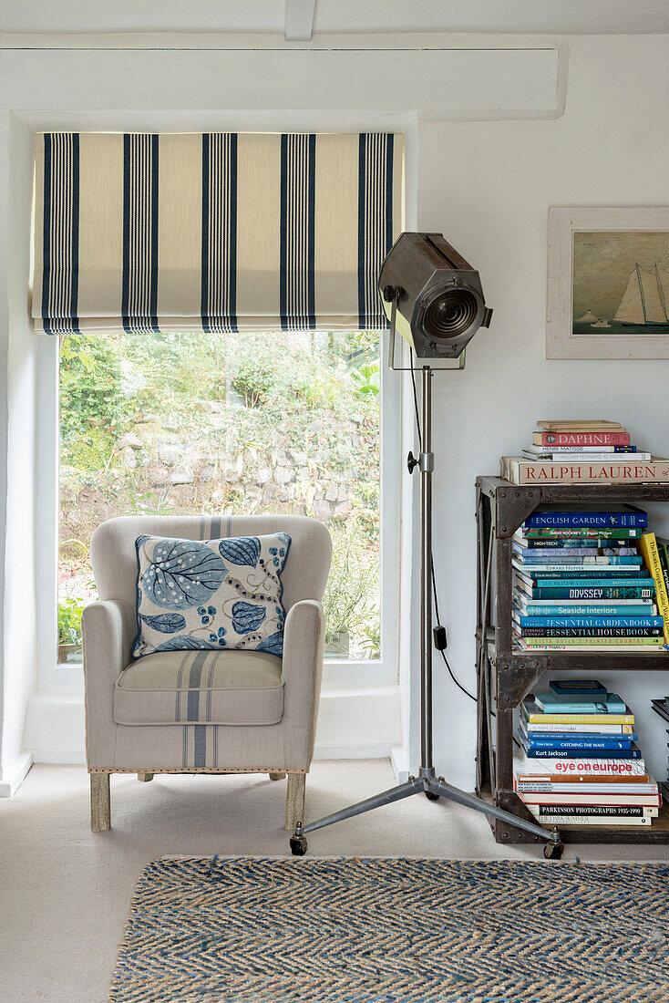 Armchair with spotlight and bookcase at window of Penzance farmhouse Cornwall England UK