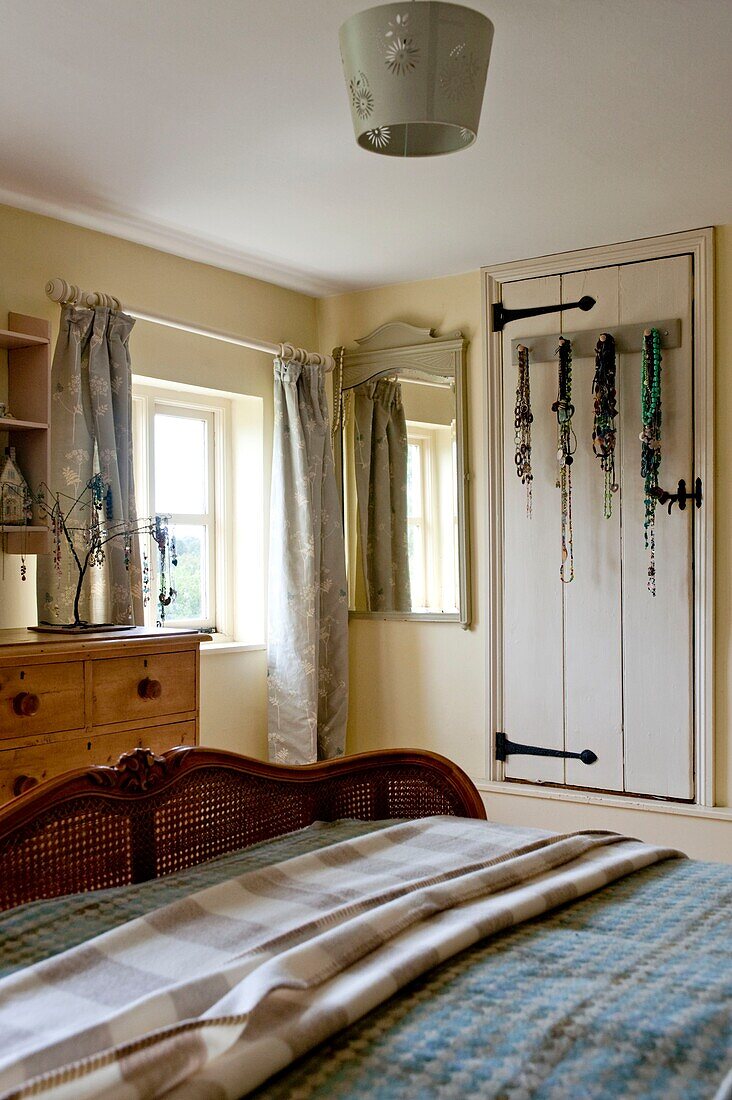 Wicker footboard on bed in room with necklaces hanging on back of door Edworth cottage Bedfordshire England UK