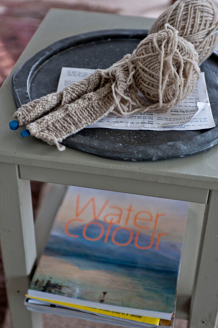 Stricknadeln und Wolle mit Aquarellbuch auf Beistelltisch in Strandhaus Cornwall England UK