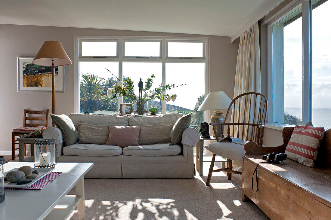 Cut flowers behind sofa in sunlit living room of beach house Cornwall England UK