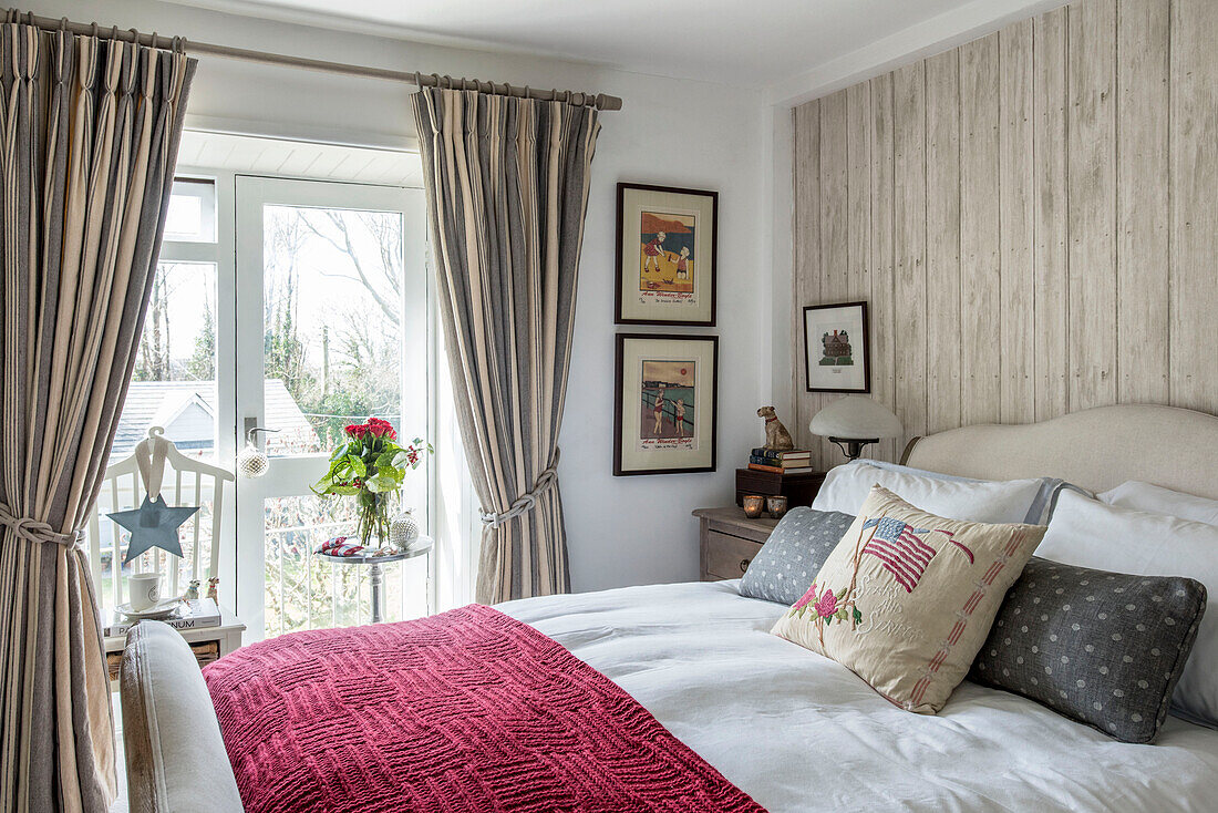 Schnittblumen im Fenster eines Schlafzimmers mit roter Decke und gerahmten Kunstwerken in einem Bauernhaus in Penzance, Cornwall, Großbritannien