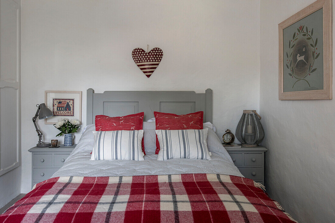 Herzförmige Sterne und Streifen über einer rot-weiß karierten Decke auf einem grauen Doppelbett in einem Bauernhaus in Penzance, Cornwall, Großbritannien