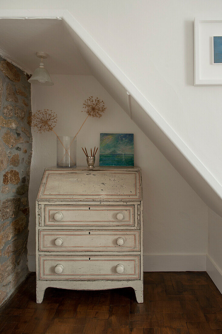 Cream painted writing bureau with exposed stone wall in Cornwall cottage UK