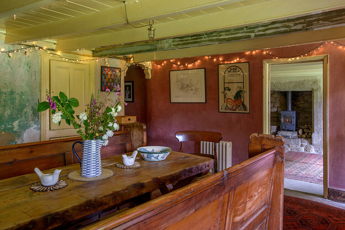 Old fashioned wooden bench seating and table with lit fairylights in Helston farmhouse Cornwall UK