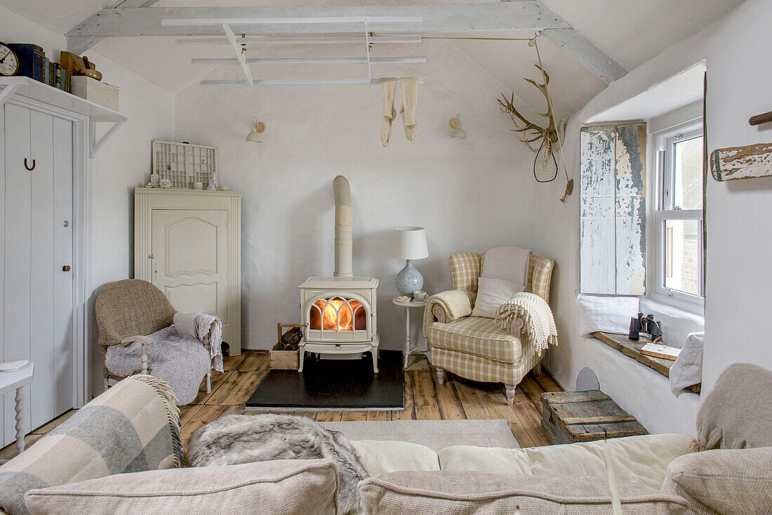 Kariertes Sofa neben einem beleuchteten Holzofen im Wohnzimmer eines Strandhauses in Marazion, Cornwall, Großbritannien