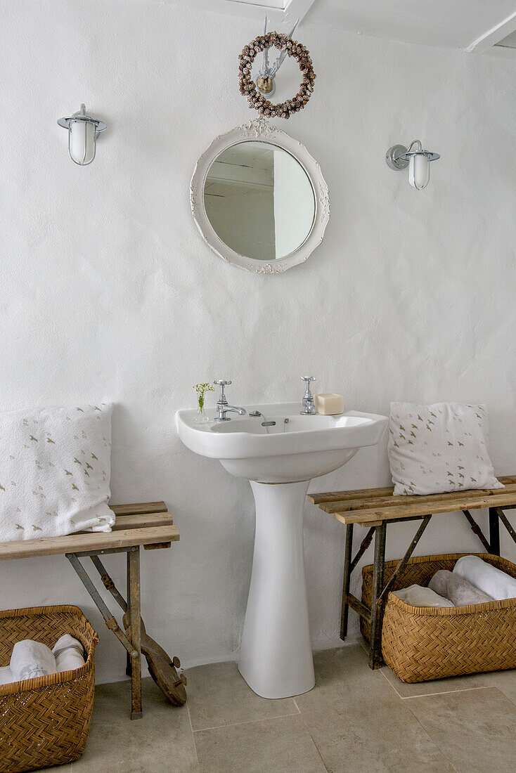 Circular mirror above pedestal basin with baskets under bench seats in Marazion beach house Cornwall UK
