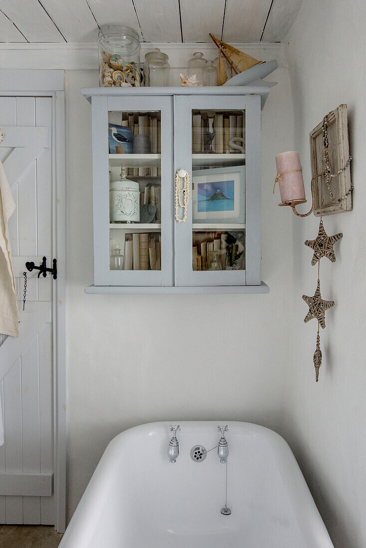 Glasschrank über einer freistehenden Badewanne in einem Strandhaus in Marazion, Cornwall, Großbritannien