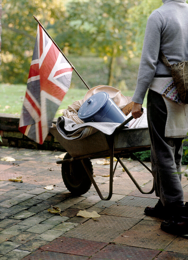 Woman pushing a wheel barrow full of household goods with Union Jack flag flying on the front