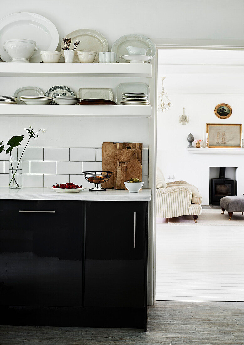 Crockery on shelves in monochrome kitchen with view to armchair at fireside in Lyme Regis home Dorset UK