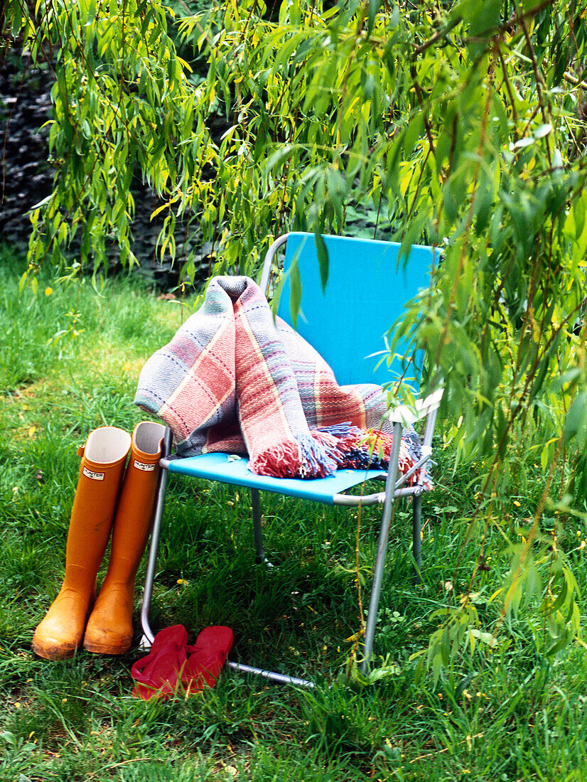 Gummistiefel und Decke mit Klappstuhl unter einem Baum am Flussufer