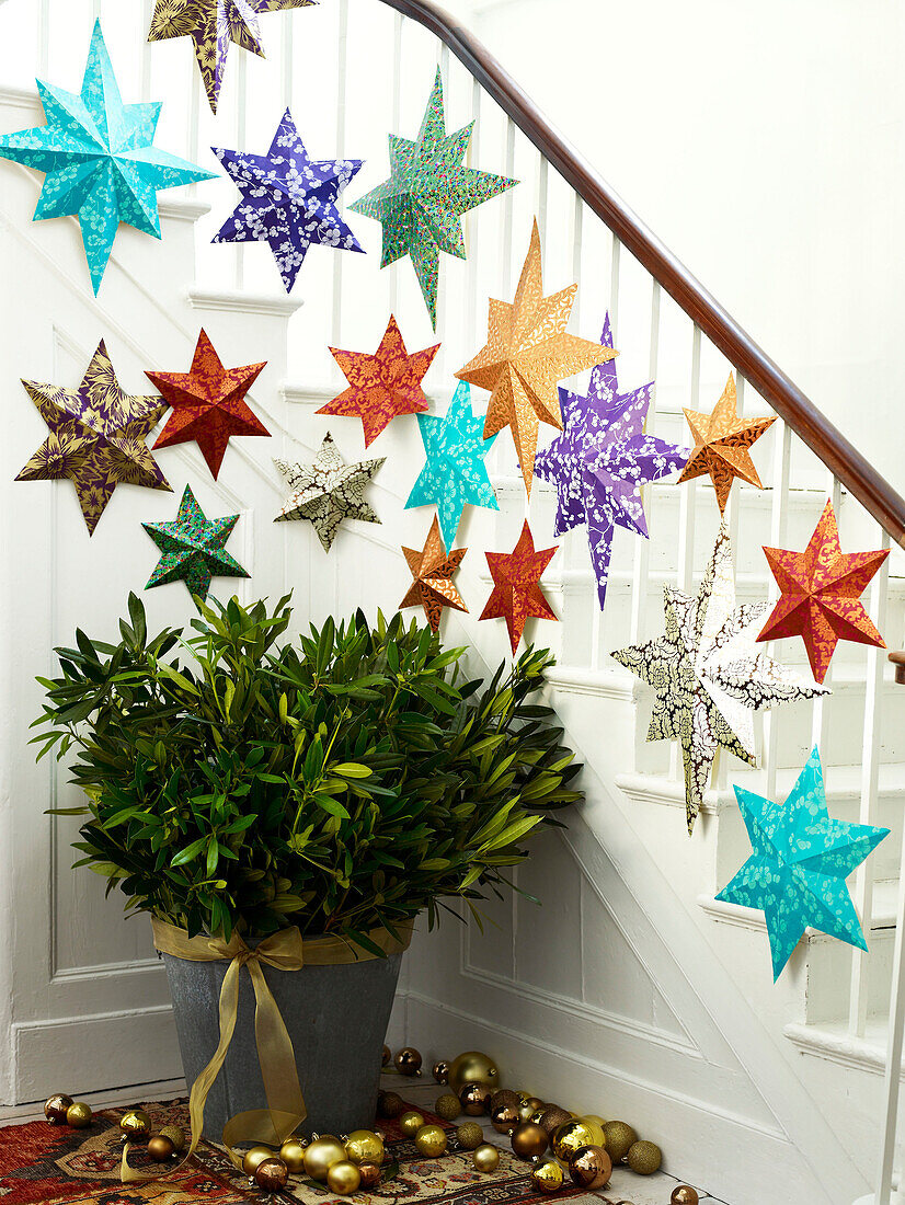 Assorted star decorations on banister with cut leaves in pot and baubles