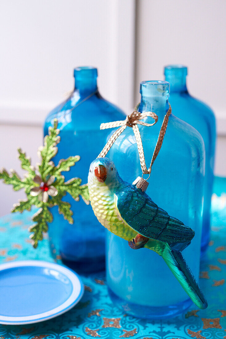 Parrot bauble tied with gold ribbon onto blue glass bottle