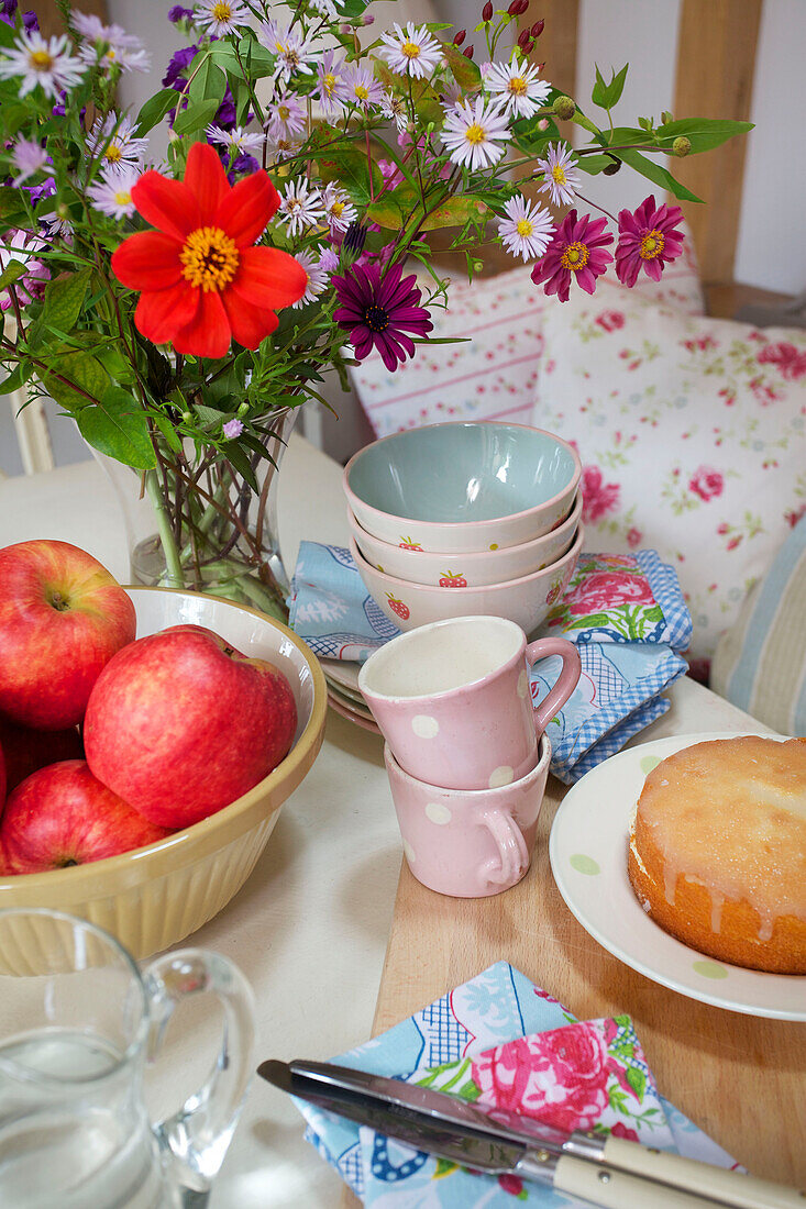 Cut flowers, apples and cake on tabletop with napkins in Sandhurst cottage, Kent, England, UK