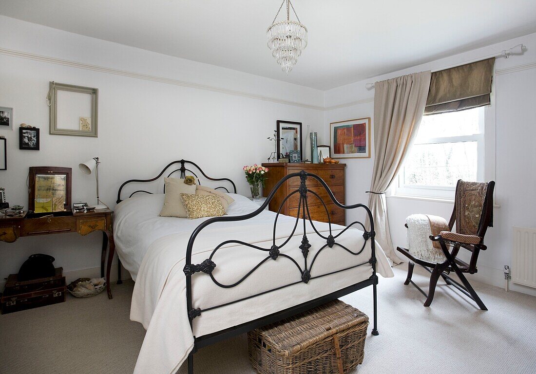 Metal worked bedframe and antique furniture in white bedroom of Tenterden home, Kent, England, UK