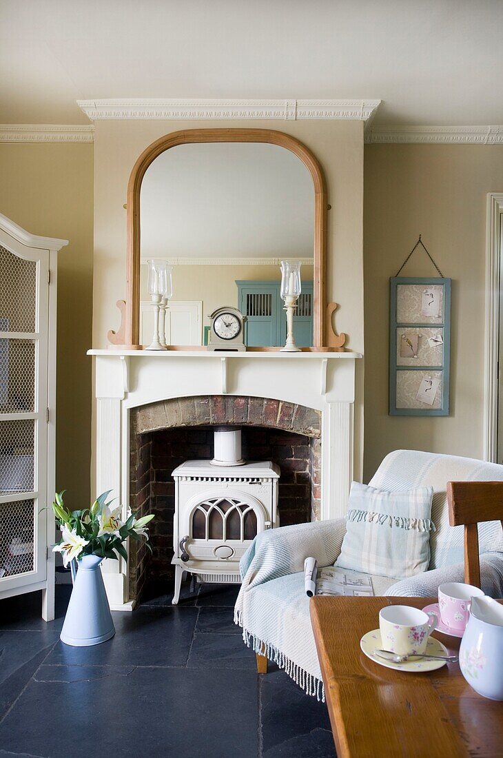 Armchair at fireplace in kitchen of timber framed cottage, Grafty Green, Kent, England, UK