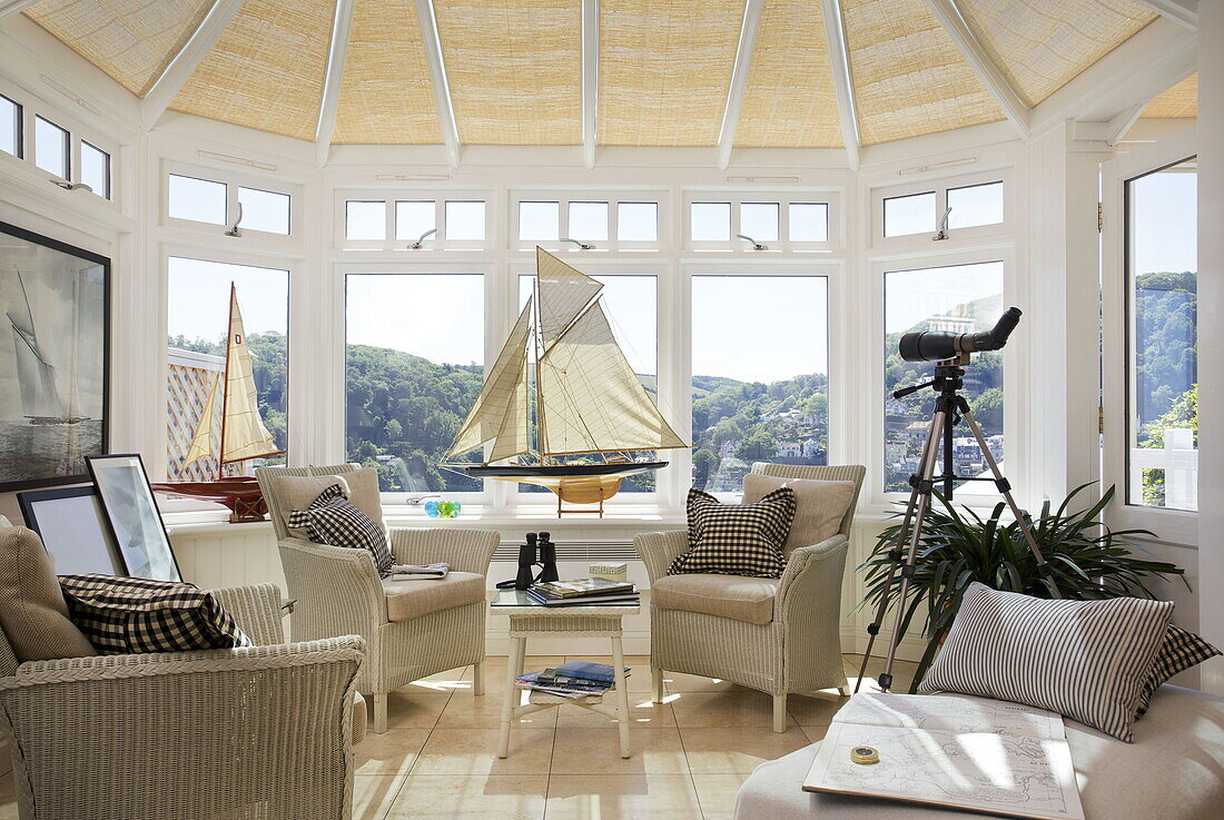 Wicker chairs with model boats in conservatory of Dartmouth home, Devon, UK