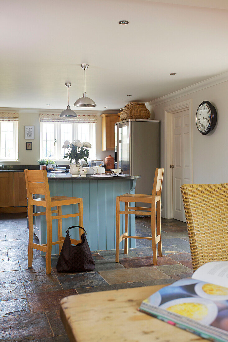 Hellblaue Kücheninsel mit hölzernen Barhockern und Tasche in einer Küche mit Schieferfußboden in einem Haus in Smarden, Kent, England