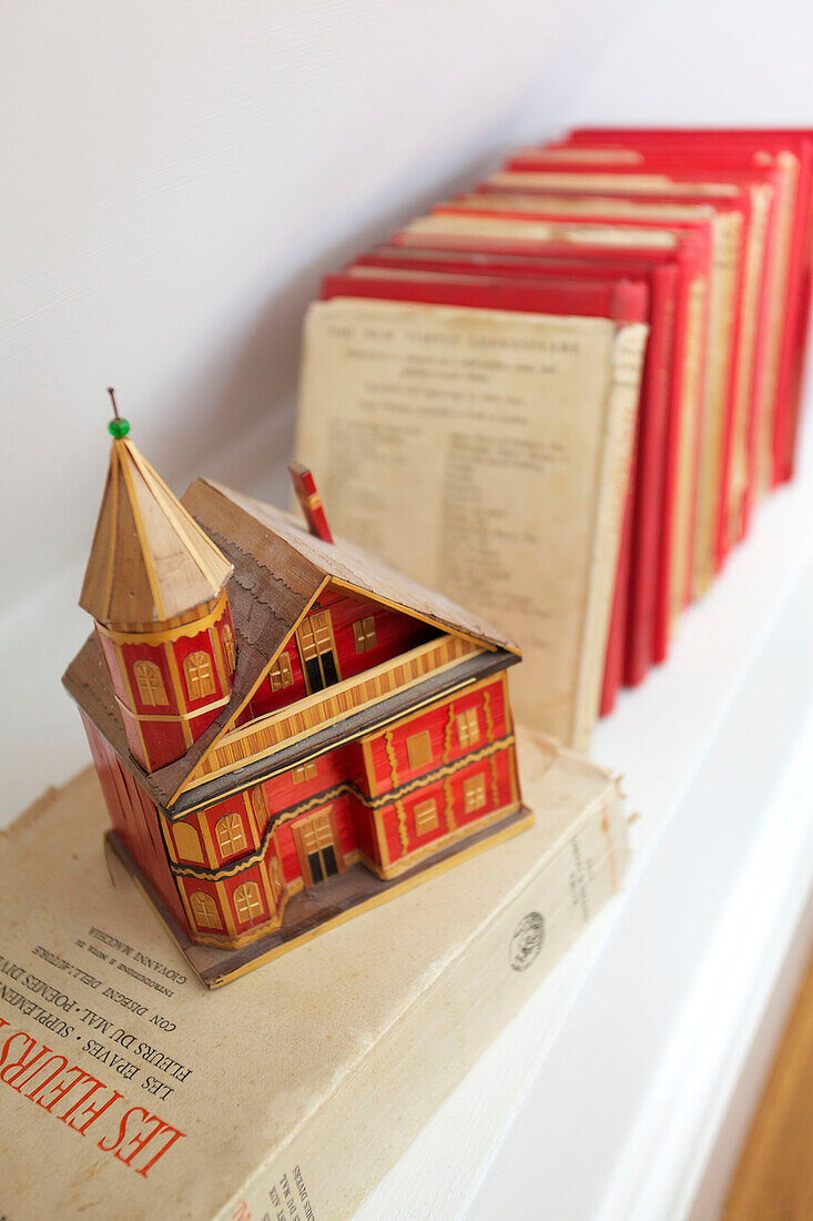 Gebundene Bücher und ein Modellhaus auf einem Regal in einem Haus in Emsworth, Hampshire, England, UK