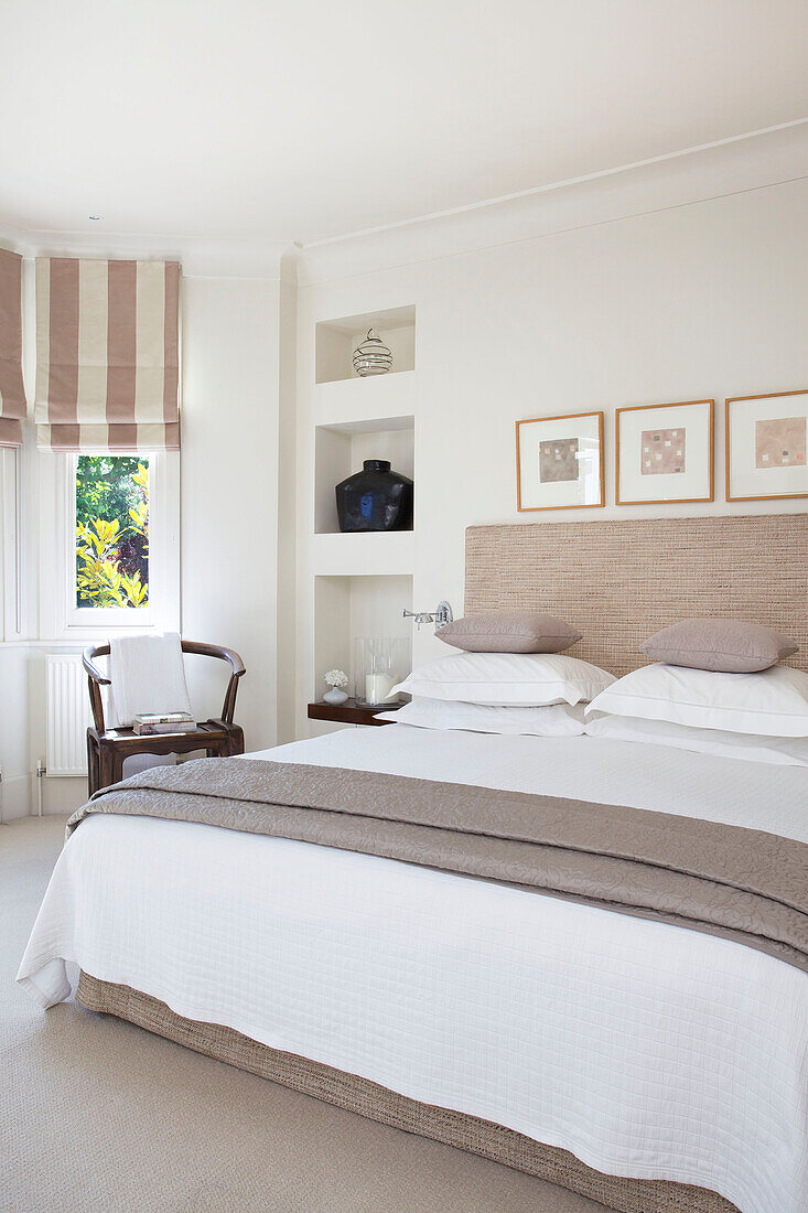 Doppelbett mit Kunstwerken und gestreiften Raffrollos in einem Haus in Wandsworth, London, England, UK